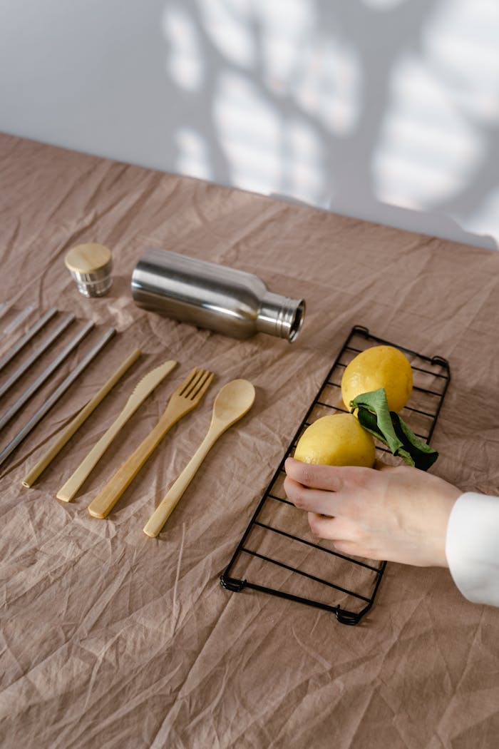 Sustainable wooden utensils with stainless flask and lemons on linen, showcasing eco-friendly dining.